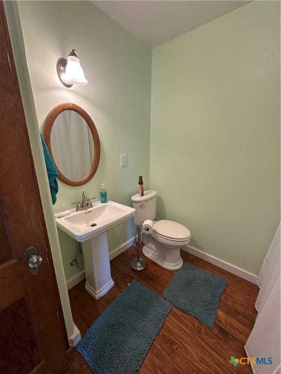 half bath featuring toilet, baseboards, and wood finished floors