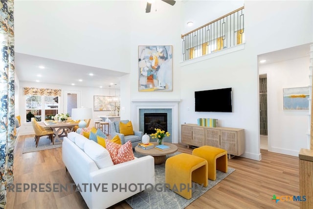 living area featuring wood finished floors, a towering ceiling, a ceiling fan, a glass covered fireplace, and baseboards