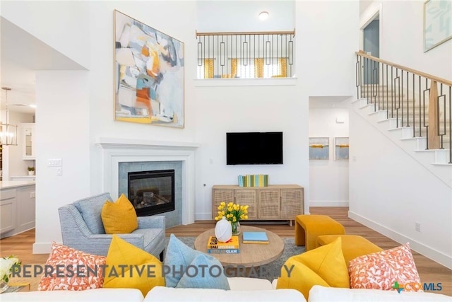 living area featuring stairway, light wood-style flooring, a tile fireplace, a towering ceiling, and baseboards