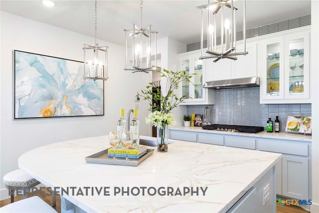 kitchen featuring under cabinet range hood, gas stovetop, decorative backsplash, and light stone counters