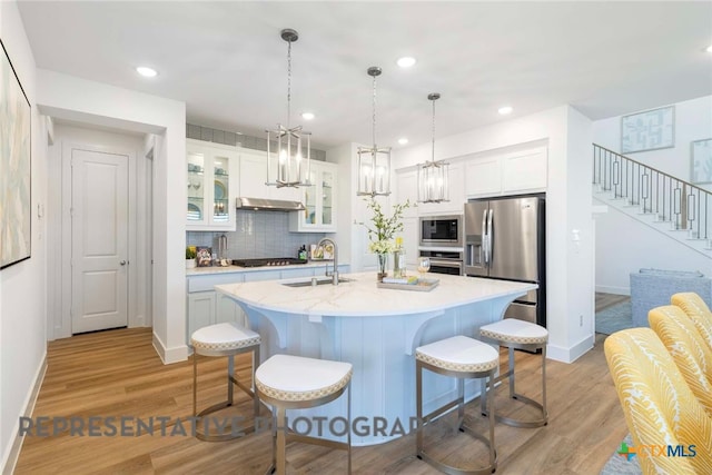 kitchen with appliances with stainless steel finishes, a sink, a kitchen bar, a center island with sink, and white cabinets