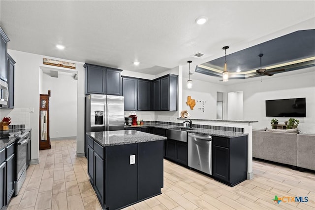 kitchen featuring a center island, a raised ceiling, ceiling fan, dark stone countertops, and stainless steel appliances