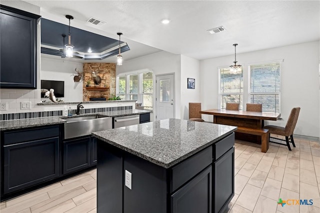 kitchen with a raised ceiling, a kitchen island, hanging light fixtures, and dark stone countertops