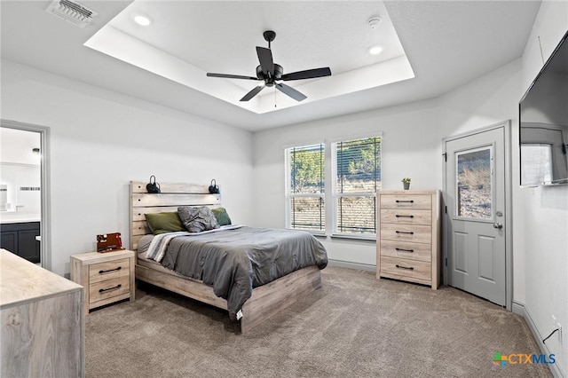 bedroom with a tray ceiling, ceiling fan, carpet flooring, and ensuite bathroom