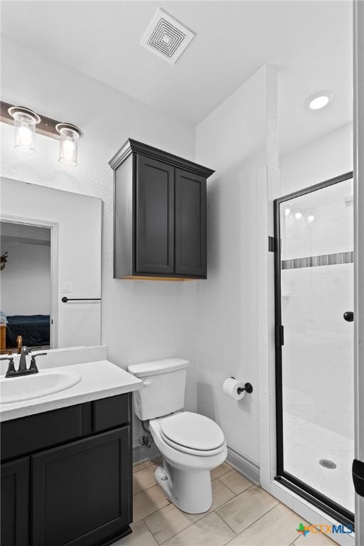 bathroom with tile patterned floors, a shower with door, vanity, and toilet