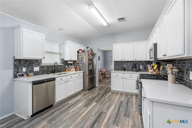 kitchen with appliances with stainless steel finishes, vaulted ceiling, sink, dark hardwood / wood-style floors, and white cabinetry