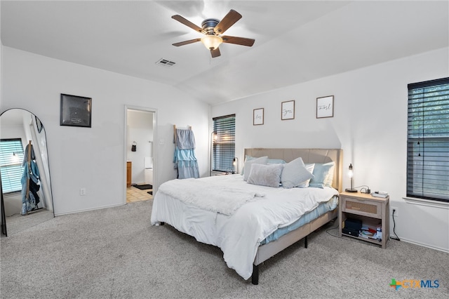 carpeted bedroom with multiple windows, ceiling fan, ensuite bath, and vaulted ceiling