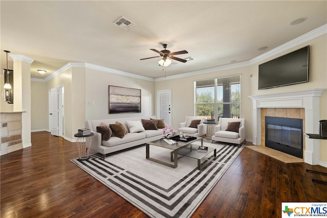 living room featuring ornamental molding, a tiled fireplace, ceiling fan, and dark hardwood / wood-style floors