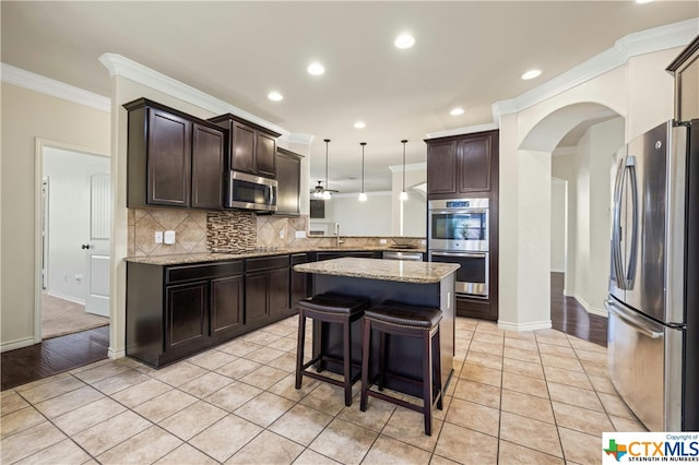 kitchen featuring stainless steel appliances, light tile patterned flooring, ornamental molding, a breakfast bar area, and pendant lighting