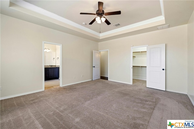 unfurnished bedroom featuring a walk in closet, crown molding, ensuite bath, a tray ceiling, and ceiling fan