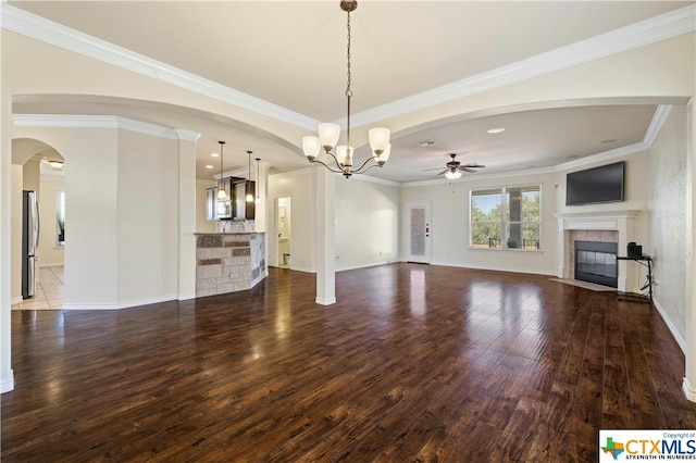 unfurnished living room with dark wood-type flooring, a tiled fireplace, ceiling fan with notable chandelier, and crown molding