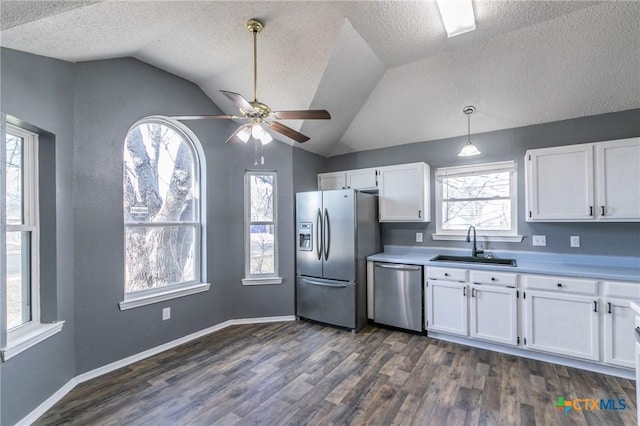 kitchen featuring appliances with stainless steel finishes, decorative light fixtures, light countertops, white cabinetry, and a sink