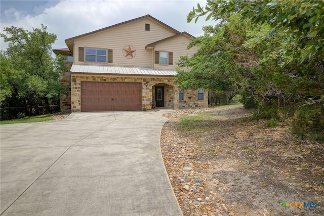 traditional-style house with a garage, metal roof, stone siding, and concrete driveway
