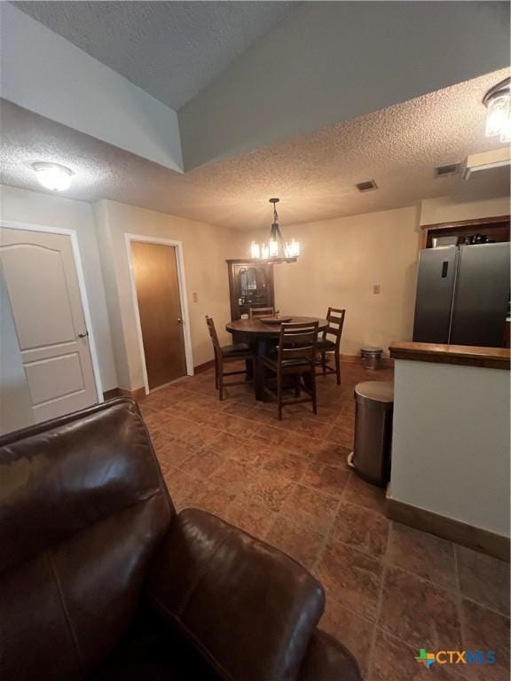 tiled dining space with a textured ceiling, baseboards, a notable chandelier, and visible vents