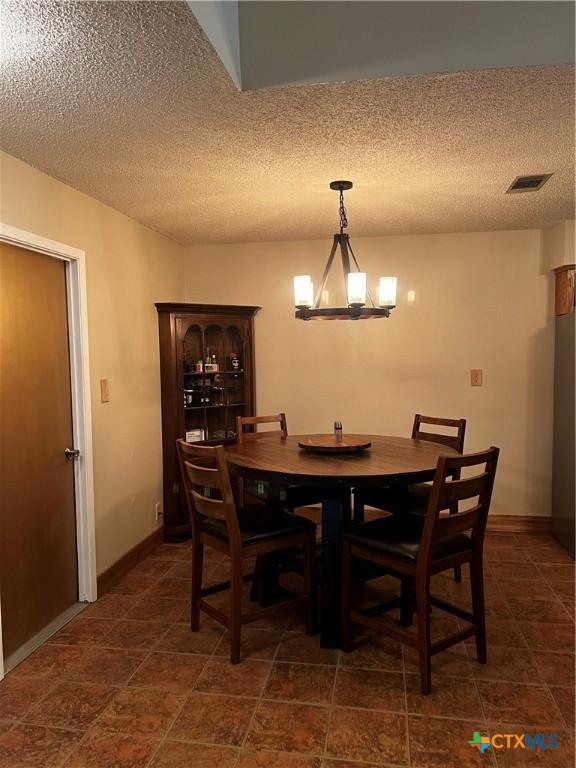 dining room with an inviting chandelier, a textured ceiling, visible vents, and baseboards