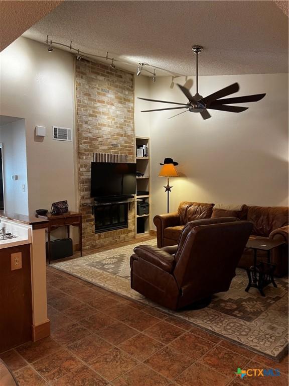 living room featuring a ceiling fan, a textured ceiling, track lighting, a fireplace, and visible vents