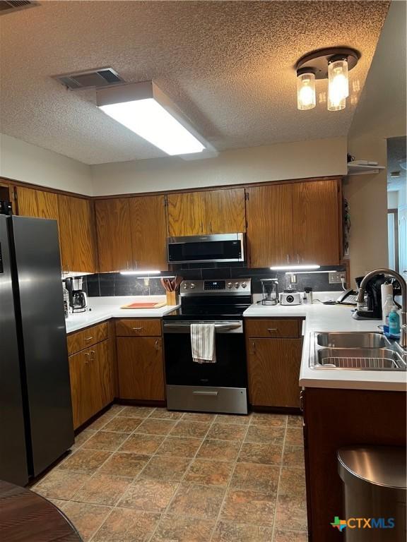 kitchen featuring brown cabinetry, stainless steel appliances, visible vents, and a sink