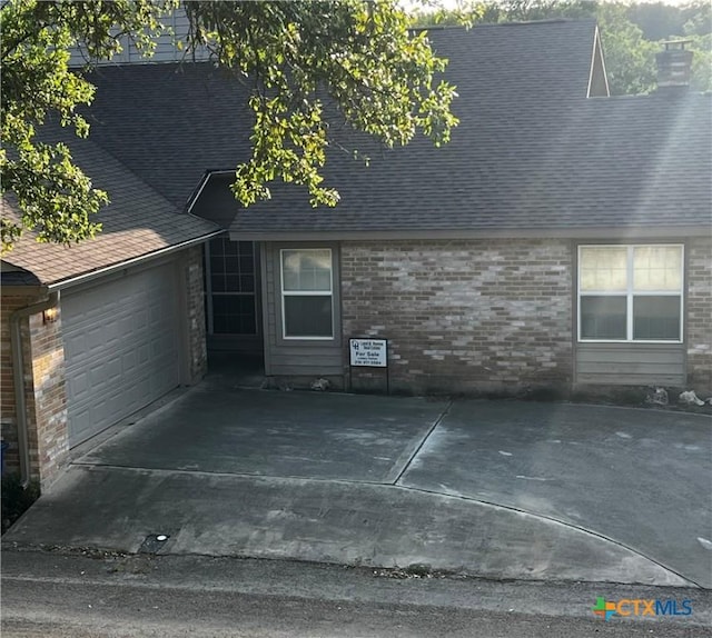 exterior space with concrete driveway, an attached garage, brick siding, and a shingled roof