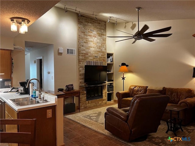 living area with high vaulted ceiling, track lighting, visible vents, a large fireplace, and ceiling fan