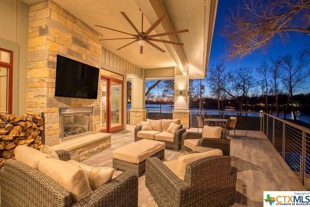 view of patio / terrace with an outdoor living space with a fireplace, ceiling fan, and a water view