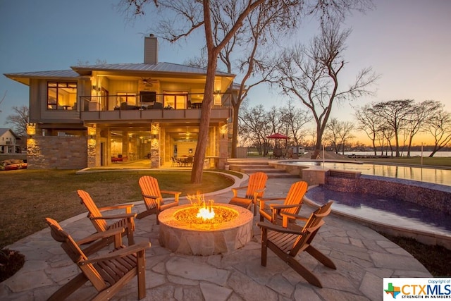 patio terrace at dusk with a fire pit and a balcony