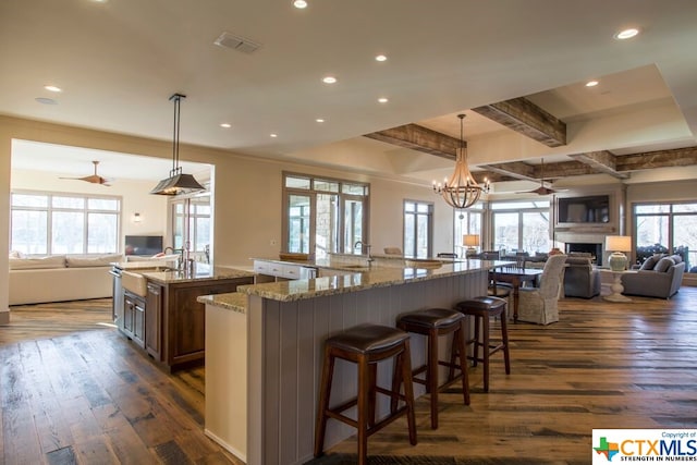 kitchen featuring a breakfast bar, light stone countertops, decorative light fixtures, a large island, and dark hardwood / wood-style flooring