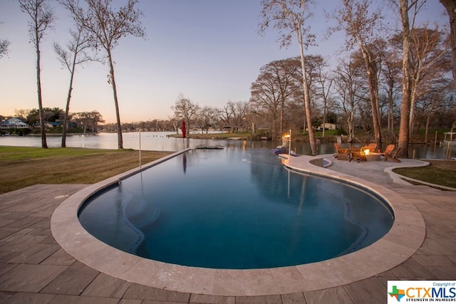 pool at dusk with a fire pit, a water view, a yard, and a patio area