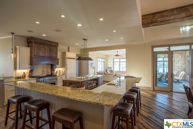 kitchen with stainless steel range with gas stovetop, dark hardwood / wood-style floors, a breakfast bar, a large island with sink, and decorative light fixtures