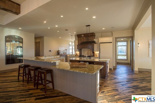 kitchen featuring a kitchen bar, dark hardwood / wood-style flooring, light stone counters, hanging light fixtures, and a large island with sink