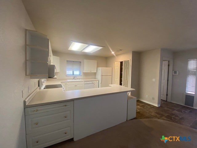 kitchen with white fridge, kitchen peninsula, sink, white cabinets, and range