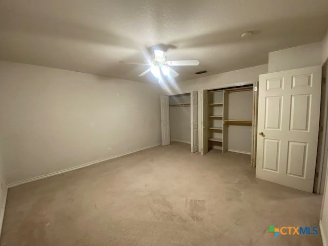 unfurnished bedroom with light carpet, ceiling fan, and multiple closets