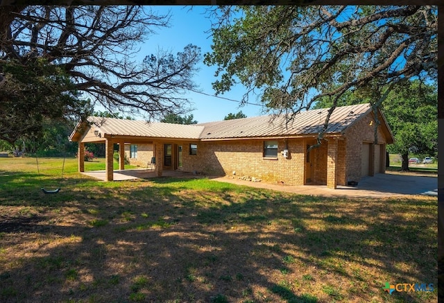 rear view of property with a garage, a yard, and a patio area