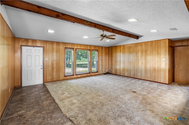 interior space featuring lofted ceiling with beams, carpet floors, a textured ceiling, wood walls, and ceiling fan