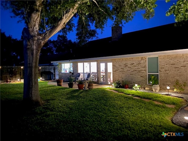 107 Savannah Dr, Victoria, TX 77904 - back of house at night with brick siding, a chimney, a patio area, and french doors