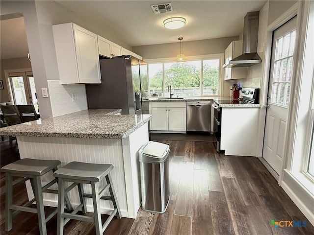 107 Savannah Dr, Victoria, TX 77904 - kitchen with wall chimney range hood, appliances with stainless steel finishes, a peninsula, tasteful backsplash, and dark wood-type flooring