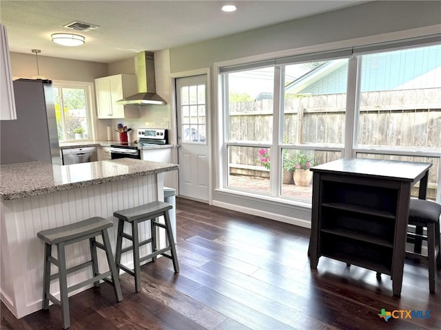 107 Savannah Dr, Victoria, TX 77904 - kitchen featuring wall chimney range hood, stainless steel appliances, white cabinetry, light stone counters, and a breakfast bar area