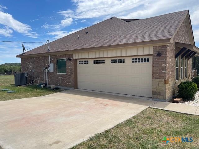 5618 County Road 3300, Kempner, TX 76539 - view of side of home featuring a shingled roof, brick siding, an attached garage, driveway, and central AC