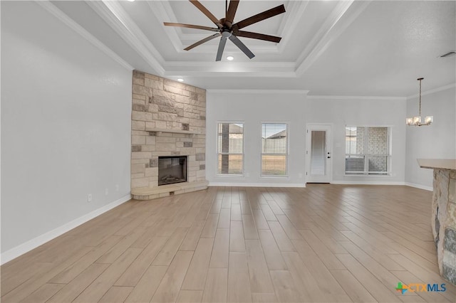 unfurnished living room with a tray ceiling, ceiling fan with notable chandelier, a stone fireplace, and ornamental molding