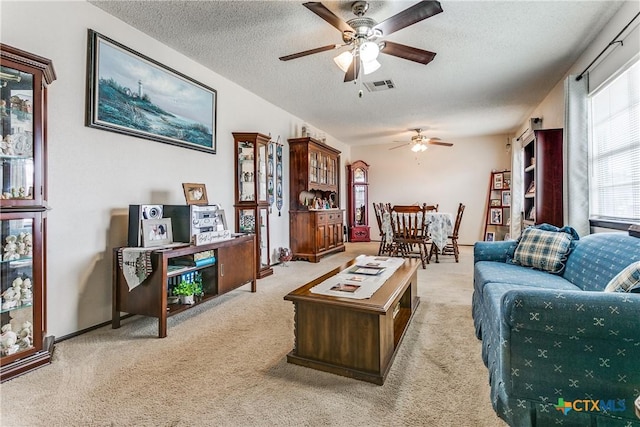 living room featuring ceiling fan, light colored carpet, and a textured ceiling