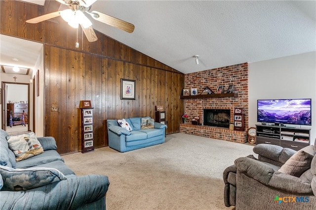 carpeted living room featuring vaulted ceiling, a textured ceiling, wooden walls, ceiling fan, and a fireplace