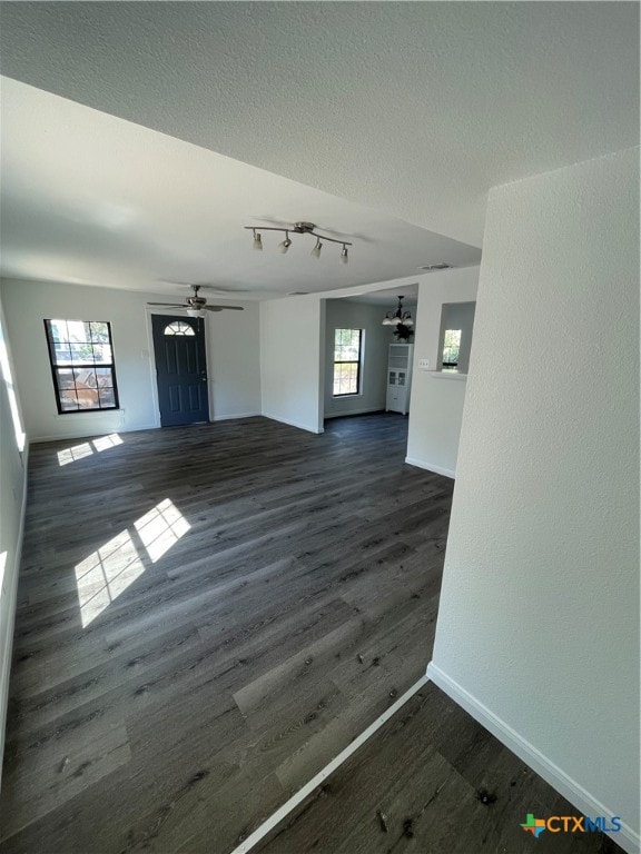 unfurnished living room featuring dark wood-type flooring, a wealth of natural light, ceiling fan, and a textured ceiling