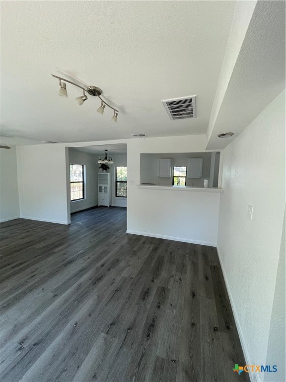 unfurnished living room featuring dark hardwood / wood-style flooring, a chandelier, track lighting, and a textured ceiling