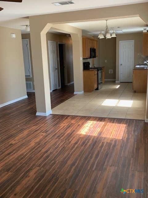 interior space featuring visible vents, ceiling fan with notable chandelier, light wood-type flooring, and baseboards