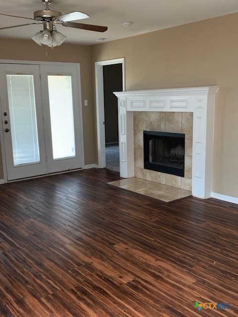 unfurnished living room with a fireplace, baseboards, dark wood-type flooring, and a ceiling fan