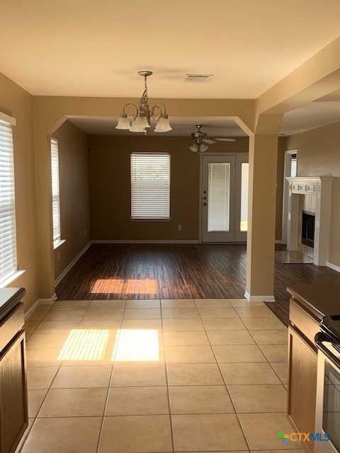 unfurnished dining area featuring visible vents, baseboards, a fireplace, tile patterned flooring, and a notable chandelier