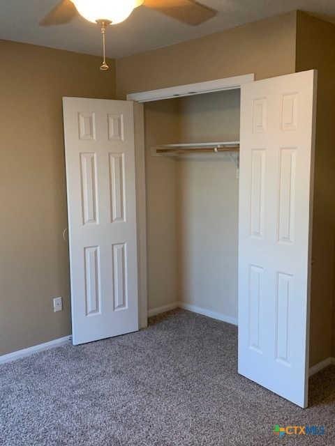 unfurnished bedroom with a closet, ceiling fan, baseboards, and carpet