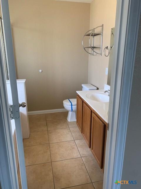 half bathroom with tile patterned floors, baseboards, toilet, and vanity