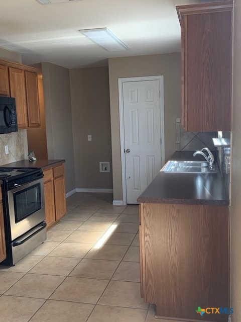 kitchen with a sink, tasteful backsplash, stainless steel range with electric cooktop, light tile patterned flooring, and black microwave