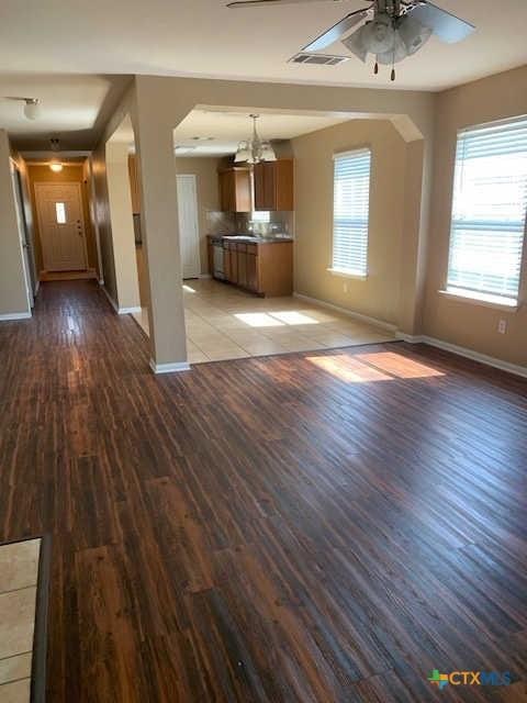 unfurnished living room with a ceiling fan, wood finished floors, visible vents, baseboards, and a sink