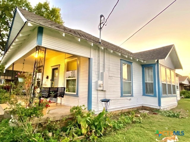 back house at dusk featuring a porch